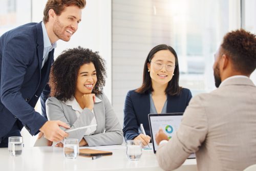 Happy diverse young businesspeople consulting together during a meeting in an office boardroom. Smi.