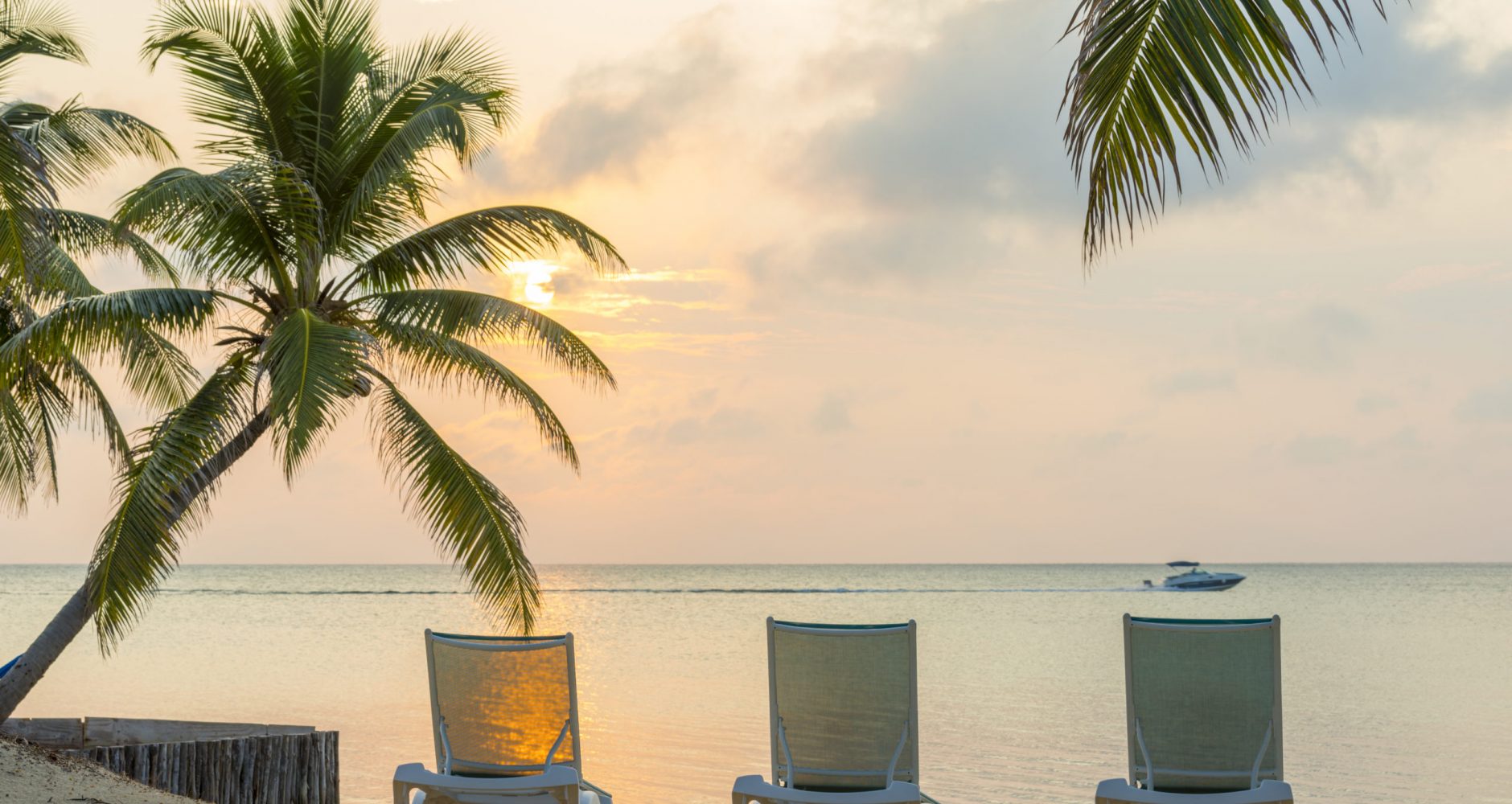 Sunrise over the ocean on dream beach vacation with palmtrees and deckchairs