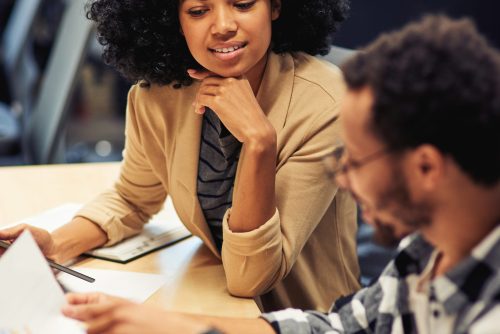 Two young diverse coworkers analyzing sales report while working together in the office. Business and teamwork concept